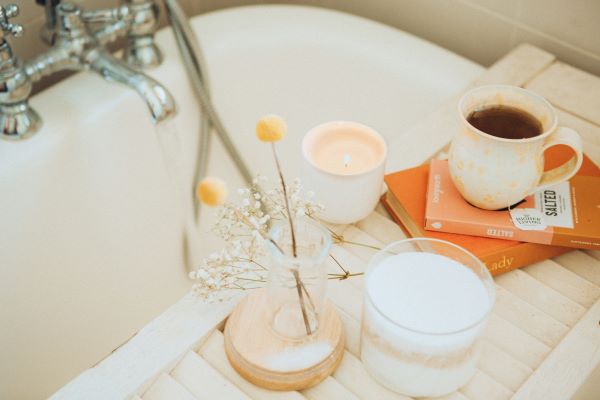 A calm self-care scene with a warm drink, candle, flowers and a bath